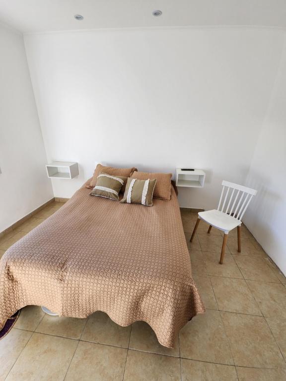 a bedroom with a bed and a white chair at Chalet con pileta y quincho, hermoso jardín in Tandil
