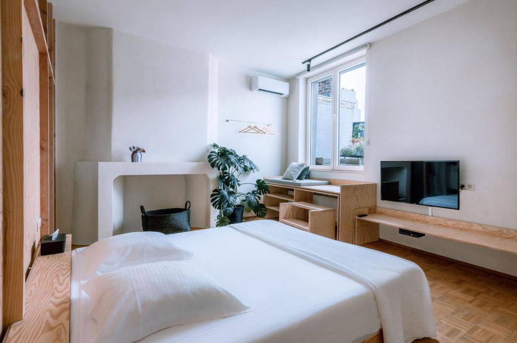 a white bedroom with a large bed and a television at Violet Suites in Ghent