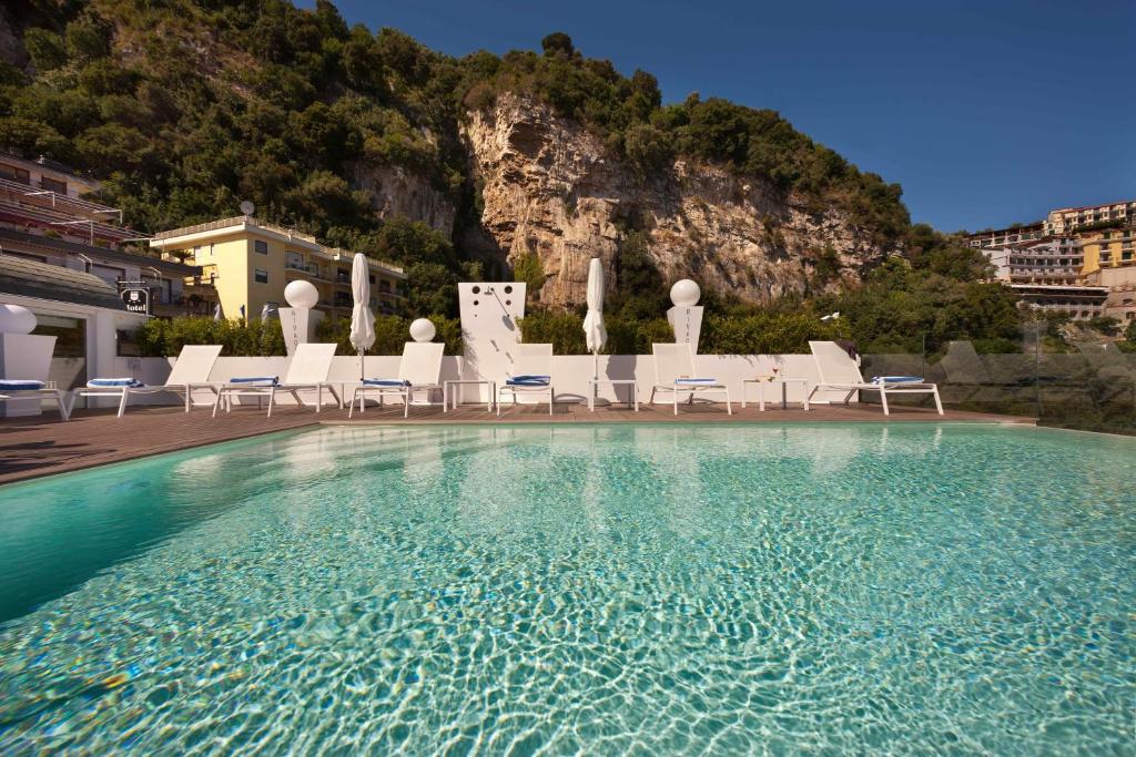 a swimming pool with chairs and a mountain in the background at Hotel Rivage in Sorrento