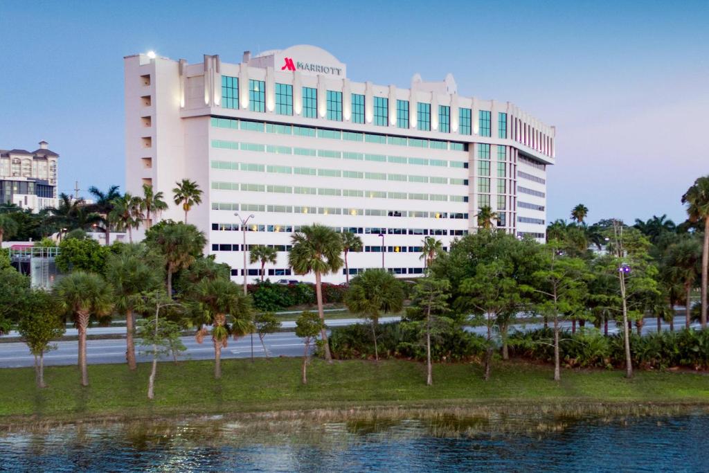 een groot wit gebouw met bomen voor een waterlichaam bij West Palm Beach Marriott in West Palm Beach