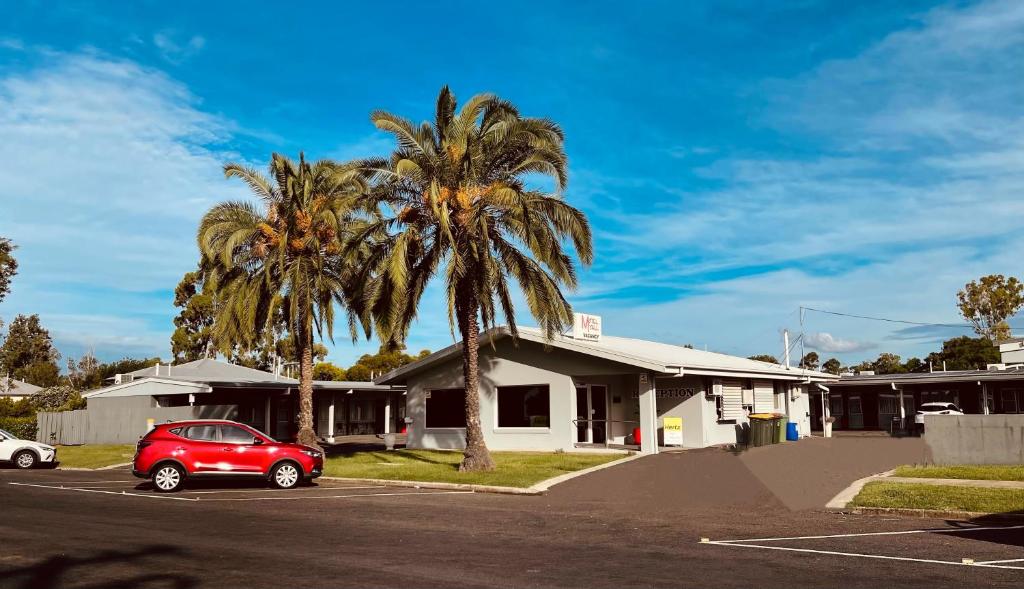 a red car parked in a parking lot with two palm trees at Motel Myall in Dalby