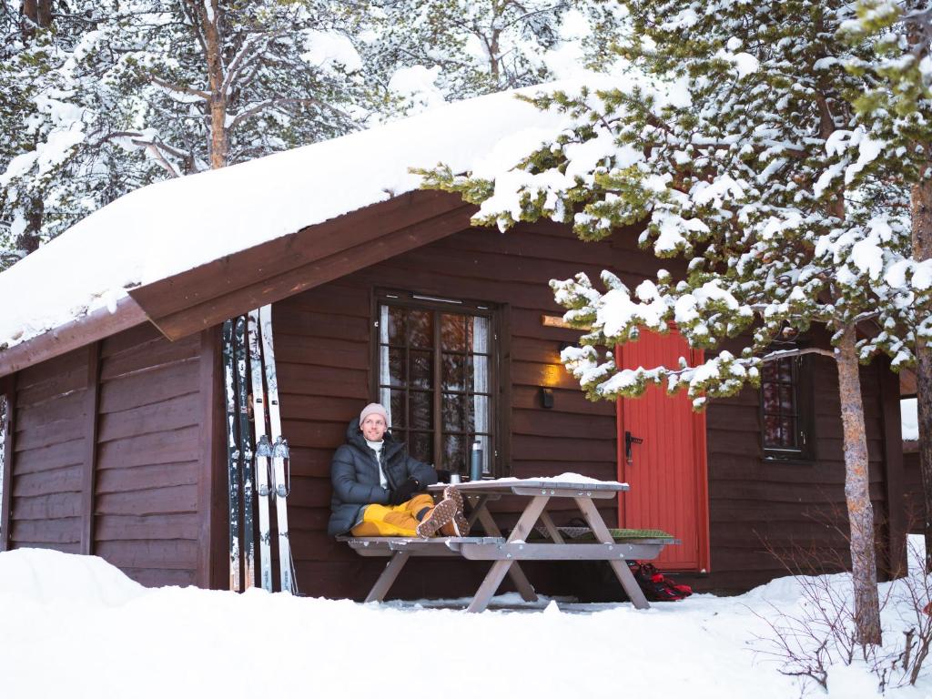 un homme assis à une table de pique-nique devant une cabine dans l'établissement Sjodalen Hyttetun og Camping, à Stuttgongfossen