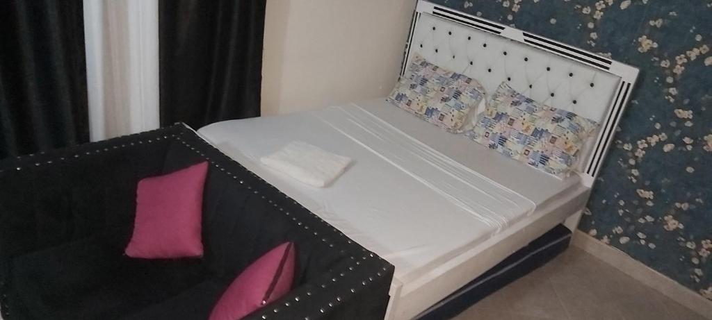 a small bed with a black and white headboard and pink pillows at Avril's studio apartment in Mombasa