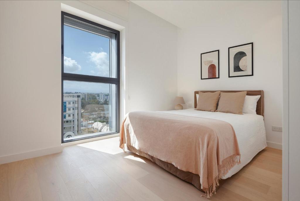 a white bedroom with a bed and a large window at Nicosia Central Park Residences in Nicosia