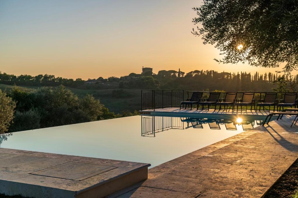een zwembad met stoelen en de zonsondergang op de achtergrond bij Palazzo Massaini - Cavarciano in Pienza