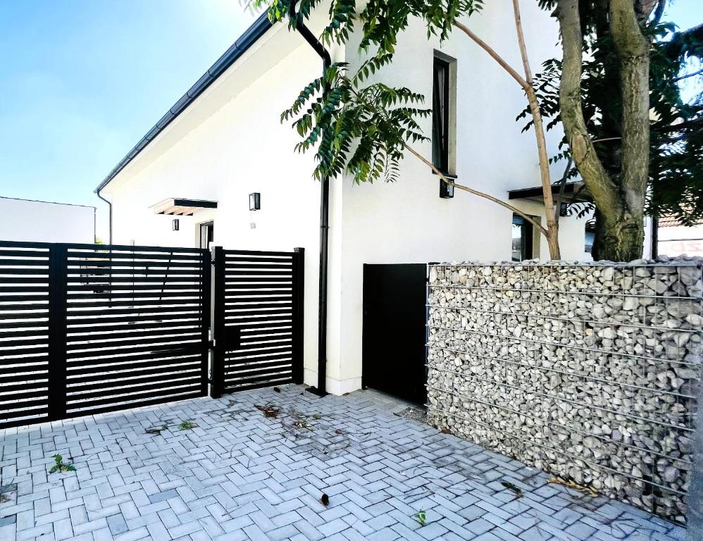 a white house with a black gate and a stone wall at House FLOW, 3 room with terrace, free 2 parking in Bratislava