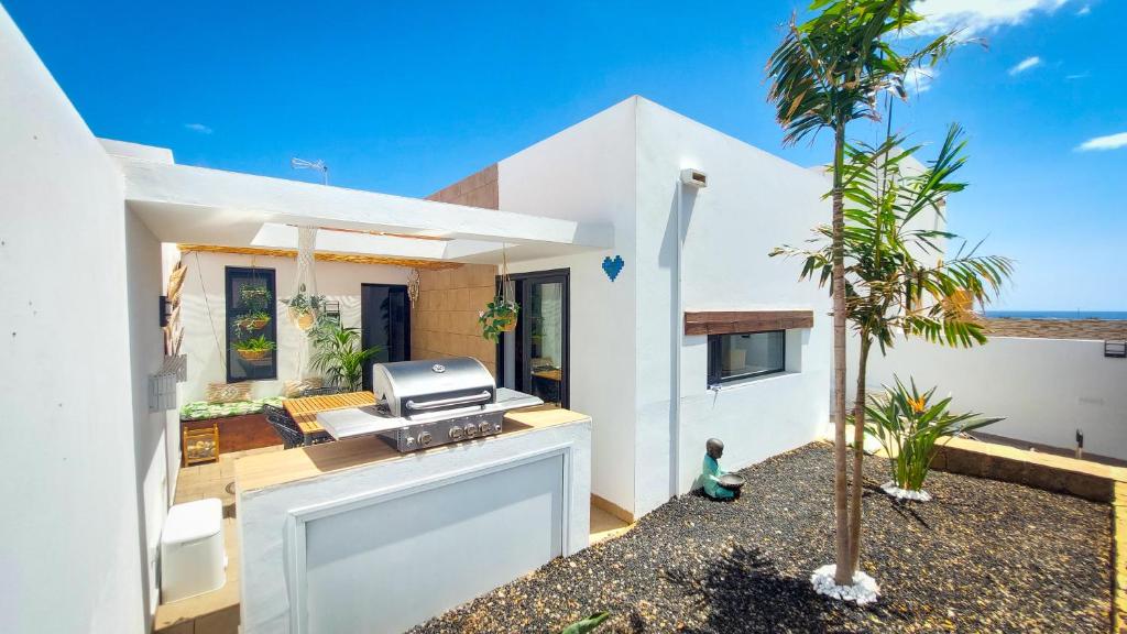 a white house with a grill and a palm tree at Villa Zephyr con piscina privada. in Gran Tarajal