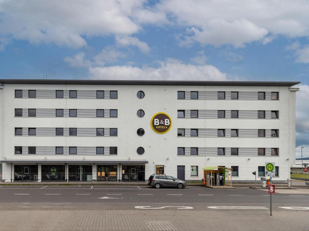 um edifício branco com um carro estacionado em frente em B&B HOTEL Frankfurt-Hahn Airport em Lautzenhausen