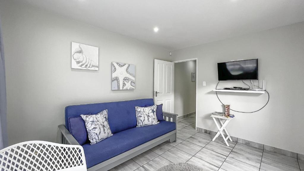 sala de estar con sofá azul y TV en Villa Dubaai, en Mossel Bay