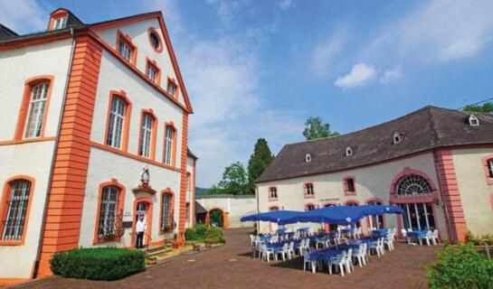 um edifício com mesas e guarda-sóis azuis num pátio em Burg Bollendorf by PRISMA em Bollendorf