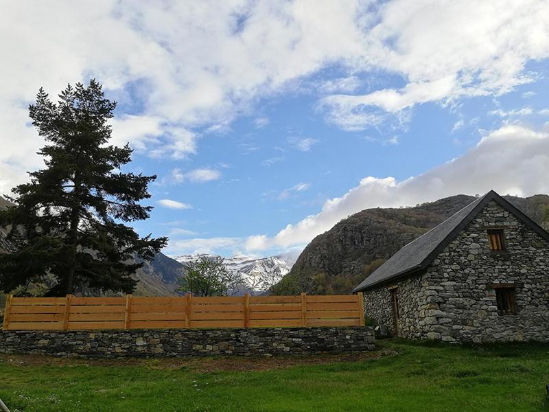 ein Holzzaun vor einem Feld mit einem Haus in der Unterkunft Ferme de Trabés *** in Gèdre