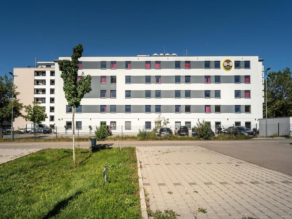 um edifício branco com uma árvore em frente em B&B Hotel Freiburg-Süd em Friburgo em Brisgóvia