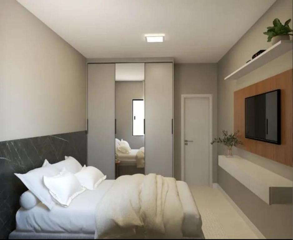 een slaapkamer met een bed met witte kussens en een televisie bij Lokehouse in Itajaí