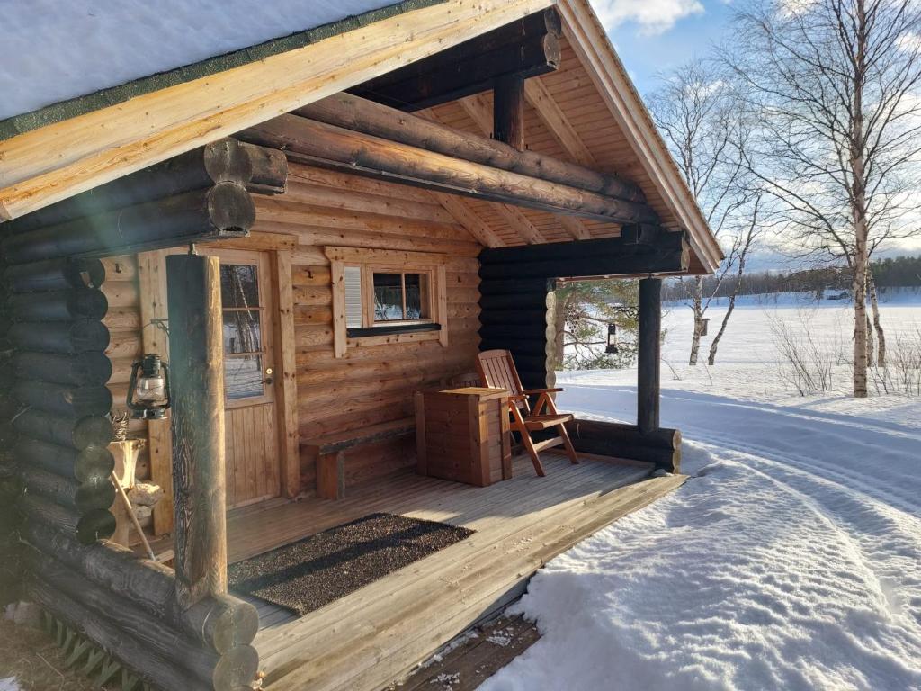 una cabaña de madera en la nieve con una silla en el porche en Lakeside Holiday Cottage near Ivalo - Minna-Carita's, en Ivalo