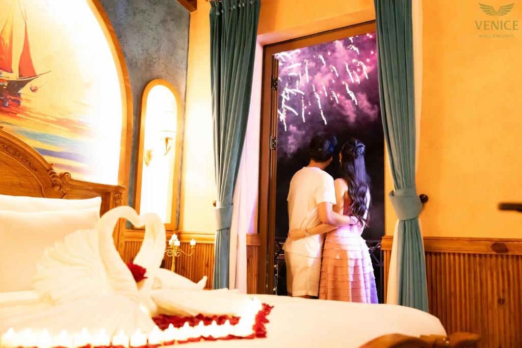 a man and a woman standing next to a bed at Venice Hotel Phu Quoc - Free Hon Thom Island Waterpark Cable Car & Sunset Town Tour in Phu Quoc