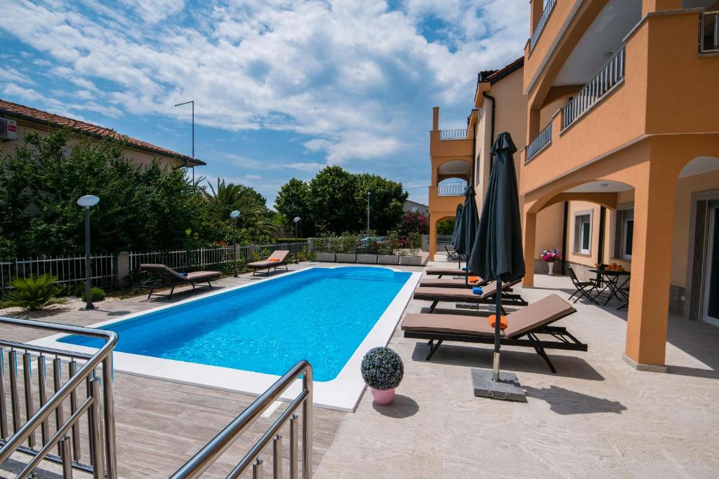 a swimming pool with chairs and umbrellas next to a building at Villa Ljubica 2 in Vodice
