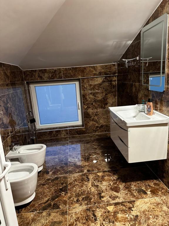 bagno con due servizi igienici, lavandino e finestra di 4 Stinët a Valbona