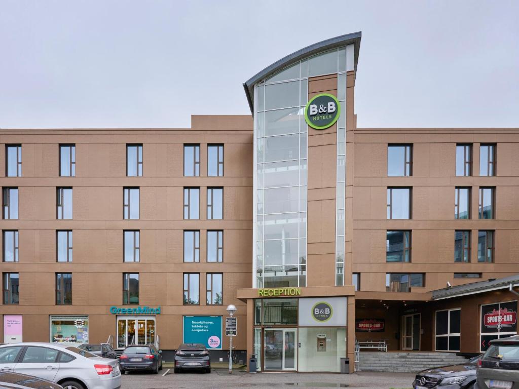 un grand bâtiment avec des voitures garées dans un parking dans l'établissement B&B HOTEL Vejle, à Vejle