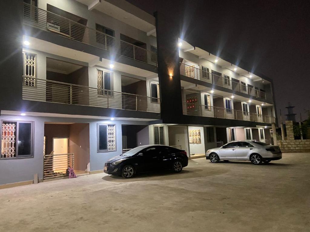 two cars parked in front of a building at night at Magic City Apartments in Kasoa