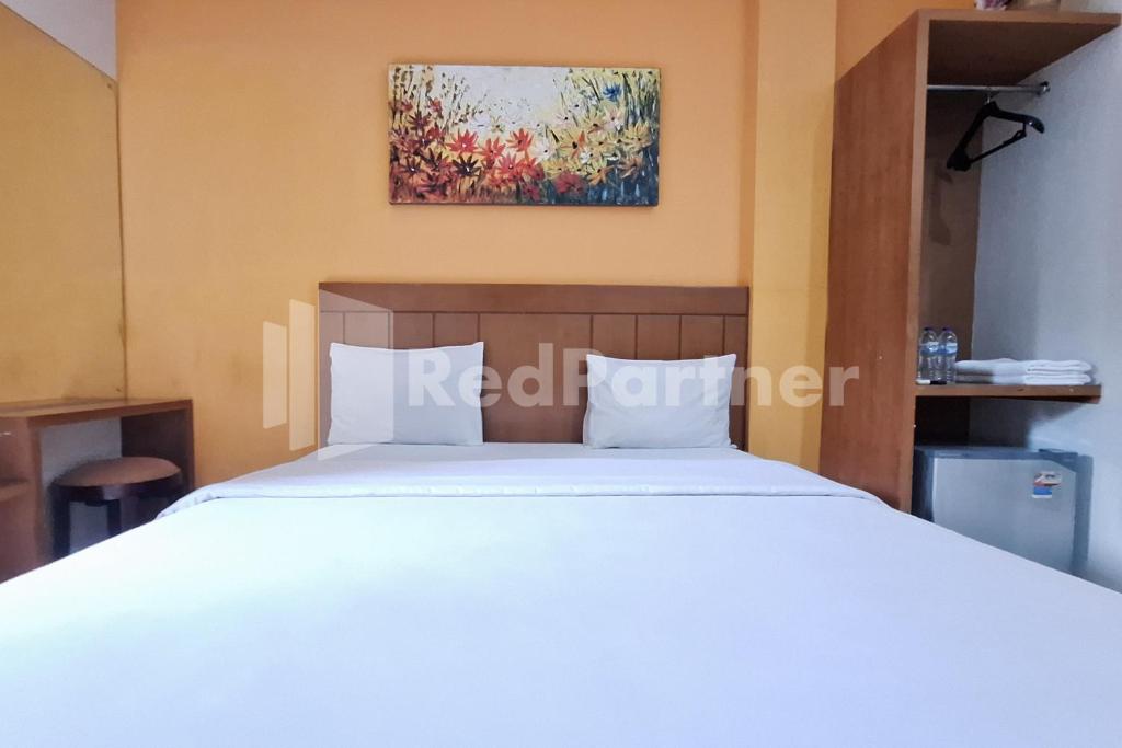 Un dormitorio con una cama blanca y un cuadro en la pared. en Nirvana Inn seturan Mitra RedDoorz, en Seturan
