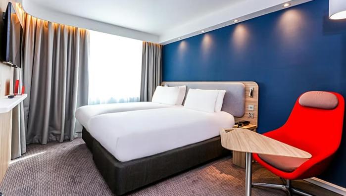 ein Schlafzimmer mit einem großen Bett und einem roten Stuhl in der Unterkunft Holiday Inn Express Caen Epron, an IHG Hotel in Épron