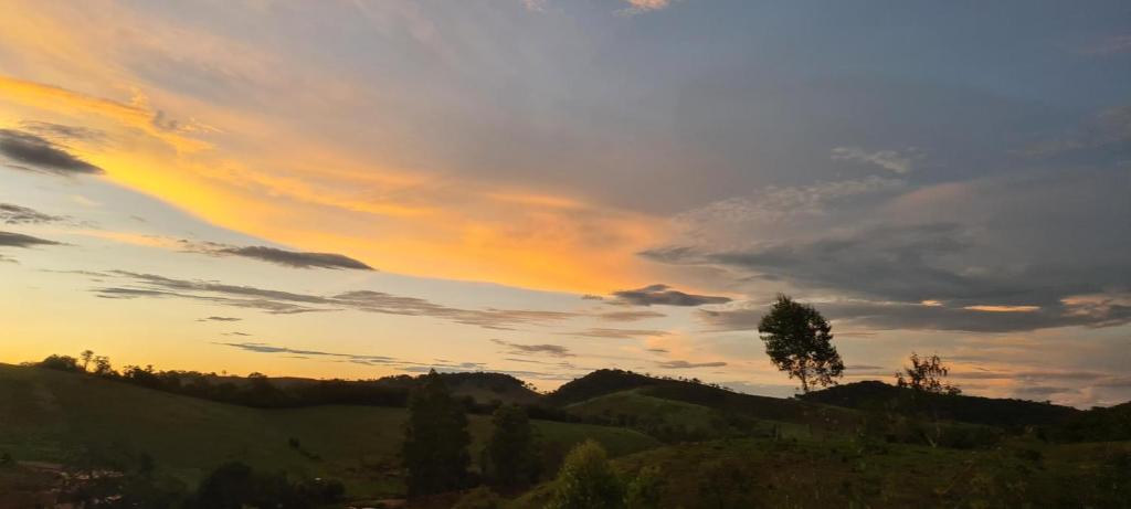 a tree on top of a hill with a sunset at Vila Monte Cunha - Chalés in Cunha