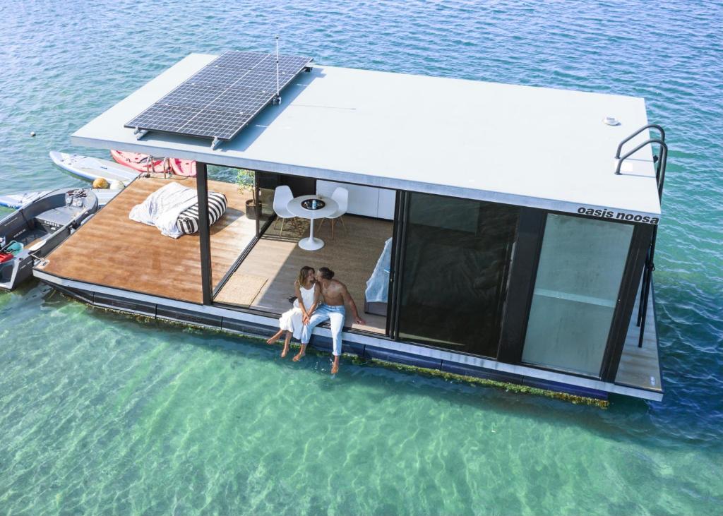 duas pessoas sentadas na parte de trás de um barco na água em oasis noosa - luxury floating eco villas em Noosa Heads