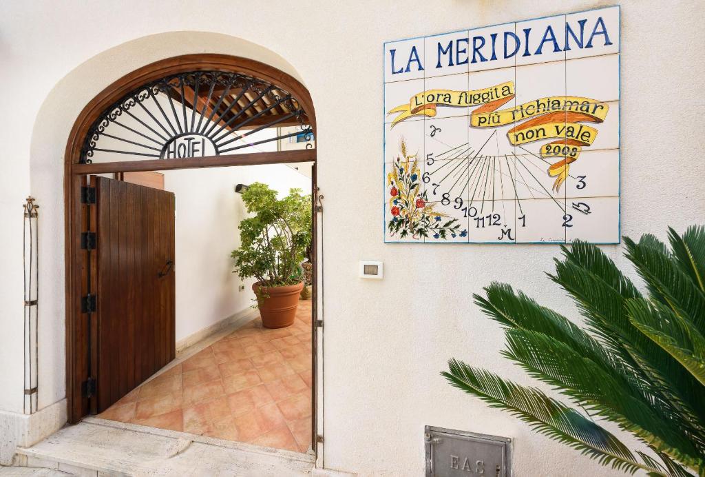 une porte menant à un bâtiment avec un panneau sur le mur dans l'établissement La Meridiana Hotel, à San Vito Lo Capo