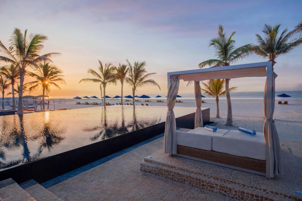 a canopy bed on the beach with palm trees at Al Baleed Resort Salalah by Anantara in Salalah