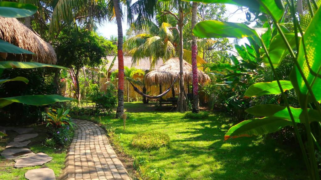 einen Weg durch einen Garten mit Palmen und einer Hütte in der Unterkunft UTOPIA in Gili Air