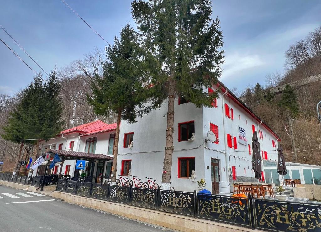 a white building with a tree next to a street at Hotel Gâlma in Moroeni