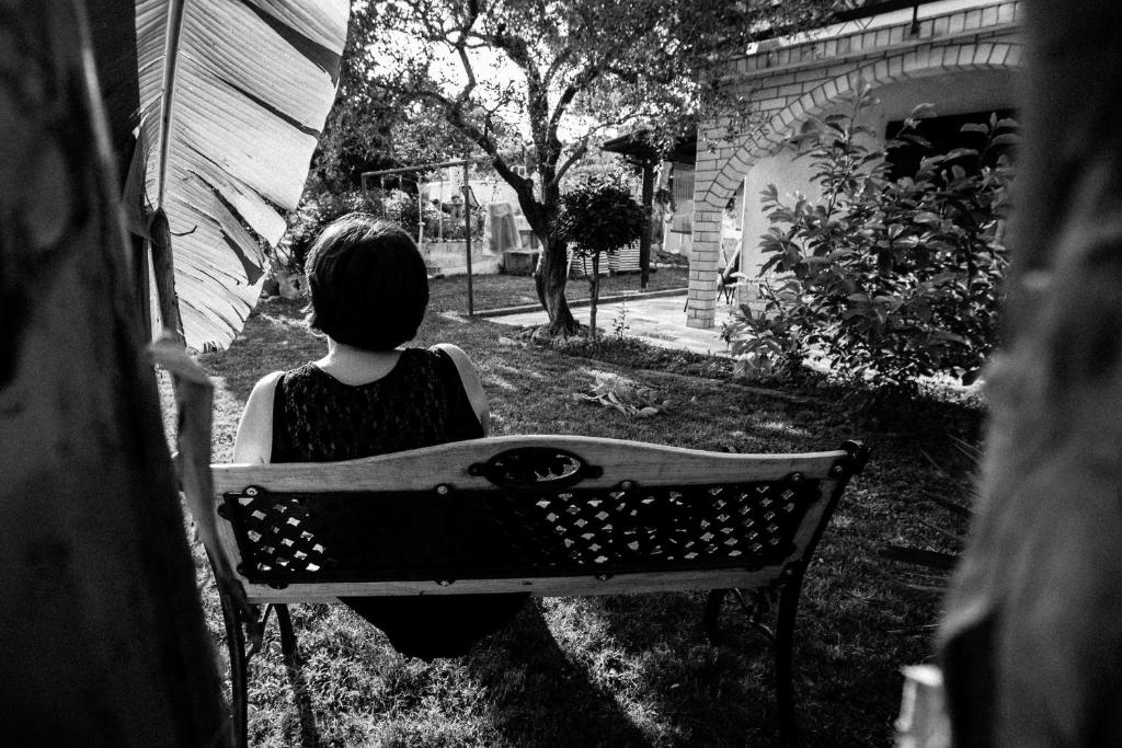 a woman sitting on a bench in a park at B&B Sobe Lušina in Sečovlje
