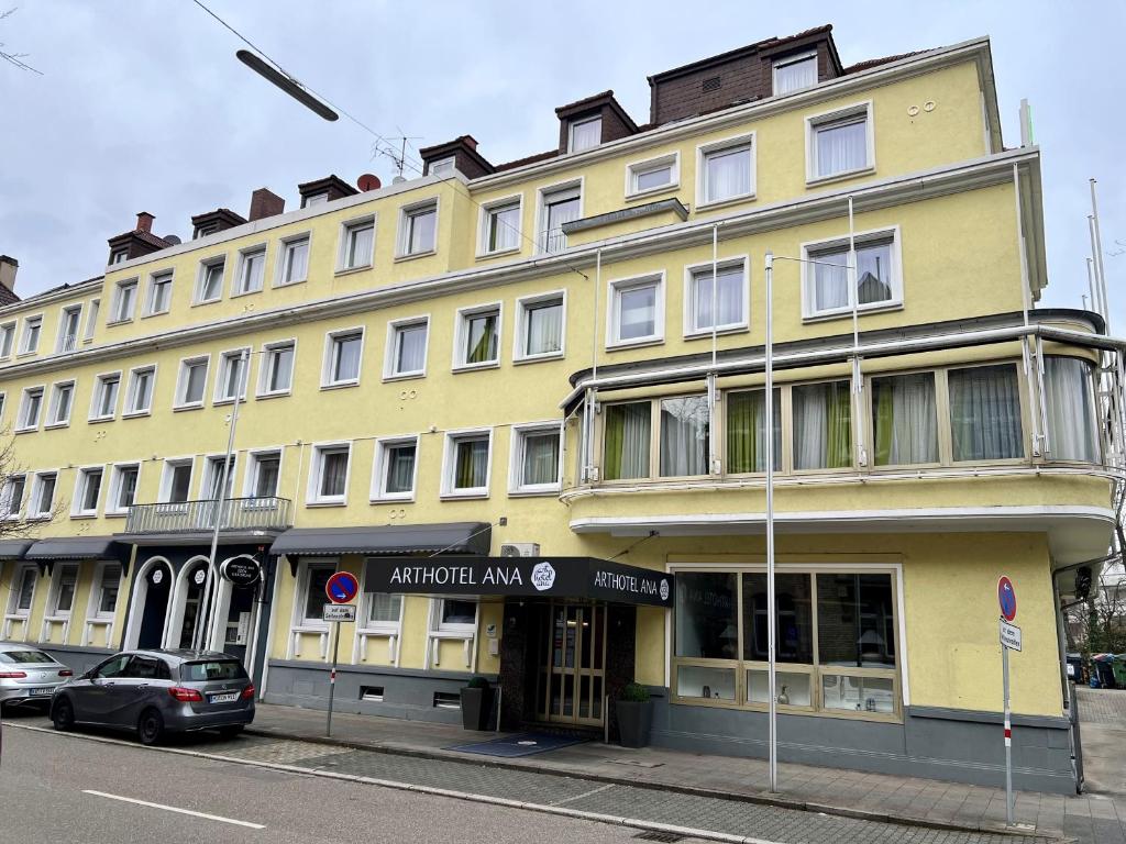 ein gelbes Gebäude auf einer Straße mit vor dem Haus geparkt in der Unterkunft Arthotel ANA Eden in Karlsruhe