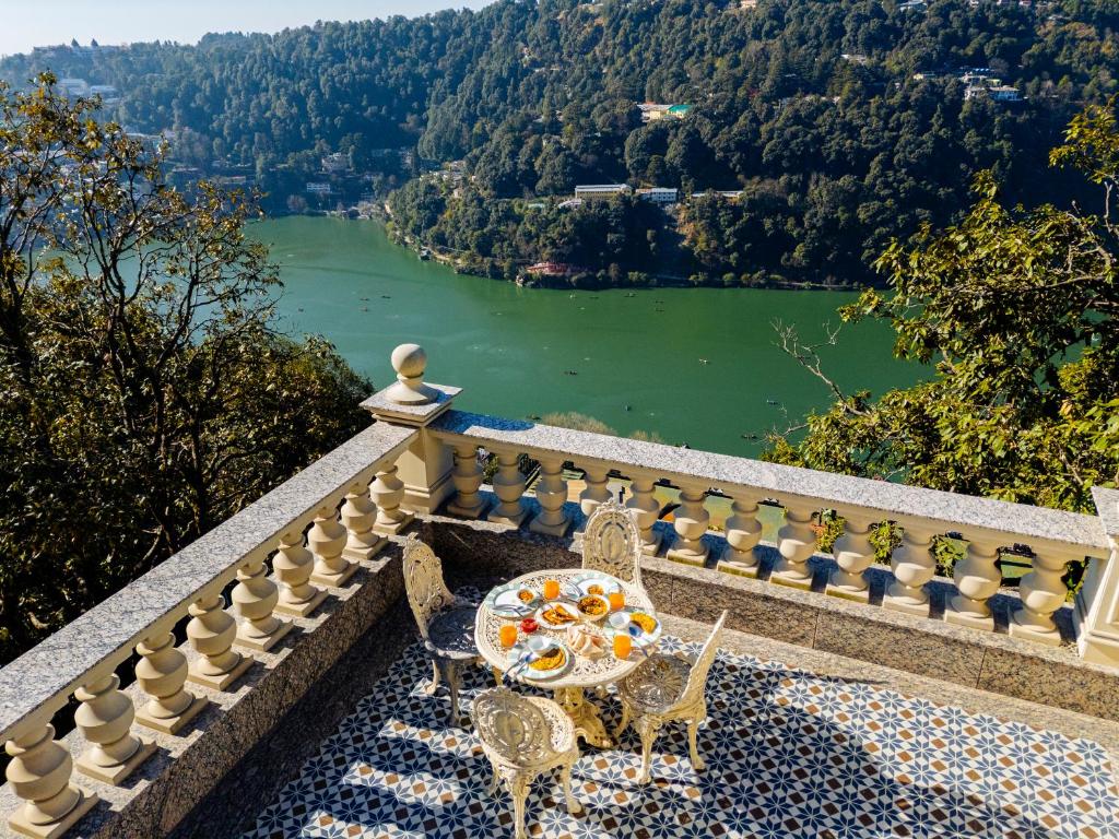 a table and chairs on a balcony with a view of a river at SaffronStays Naiintara in Nainital