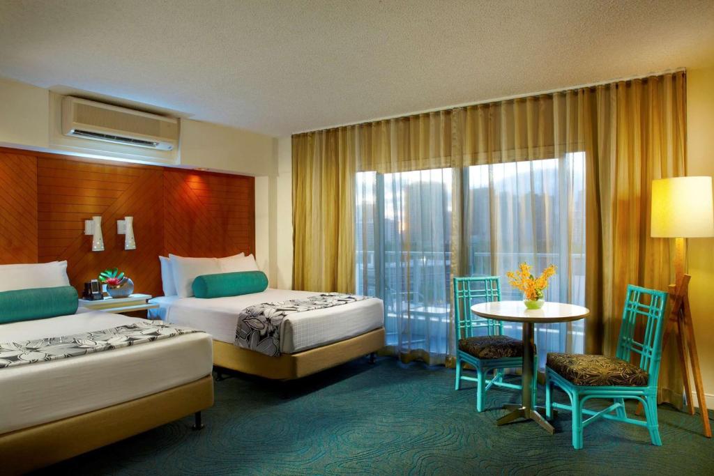 a hotel room with two beds and a table and chairs at Oasis Hotel Waikiki in Honolulu