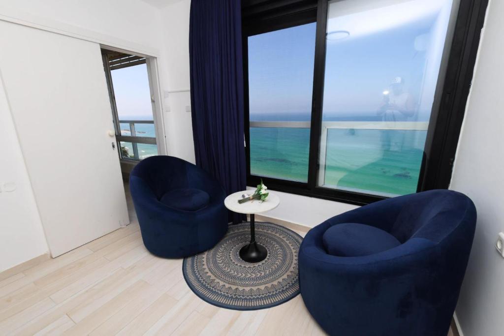 two blue chairs and a table in a room with large windows at קו ראשון לים in Netanya