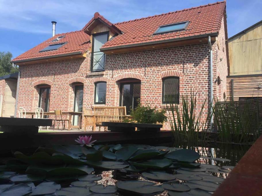 a brick house with a pond in front of it at Fermette cosy, Bain nordique &amp; Baby foot in Fromelles