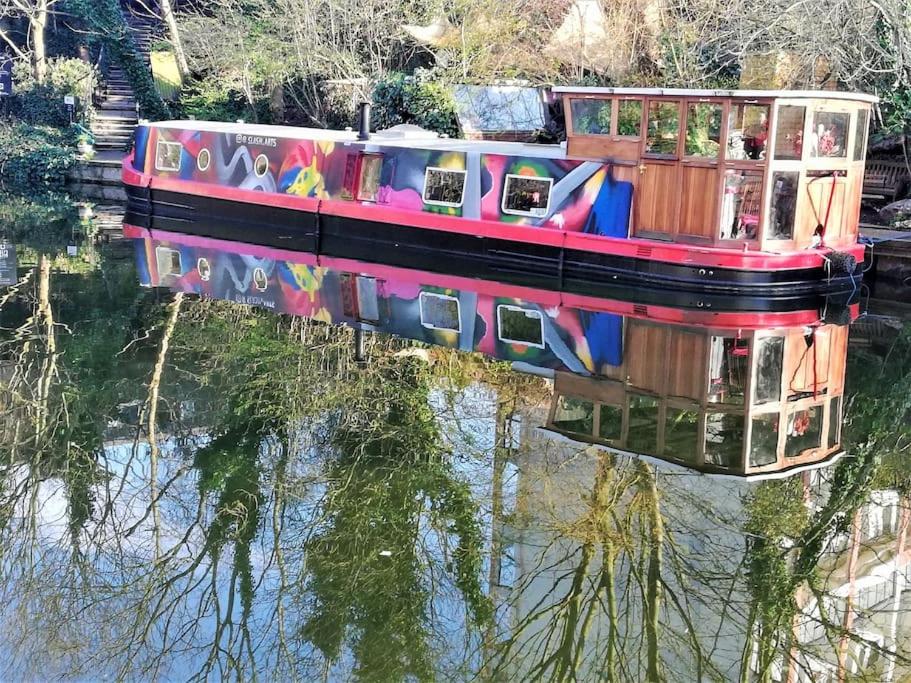 a colorful boat on a river with its reflection in the water at Slash Arts houseboat on secluded mooring in central London in London