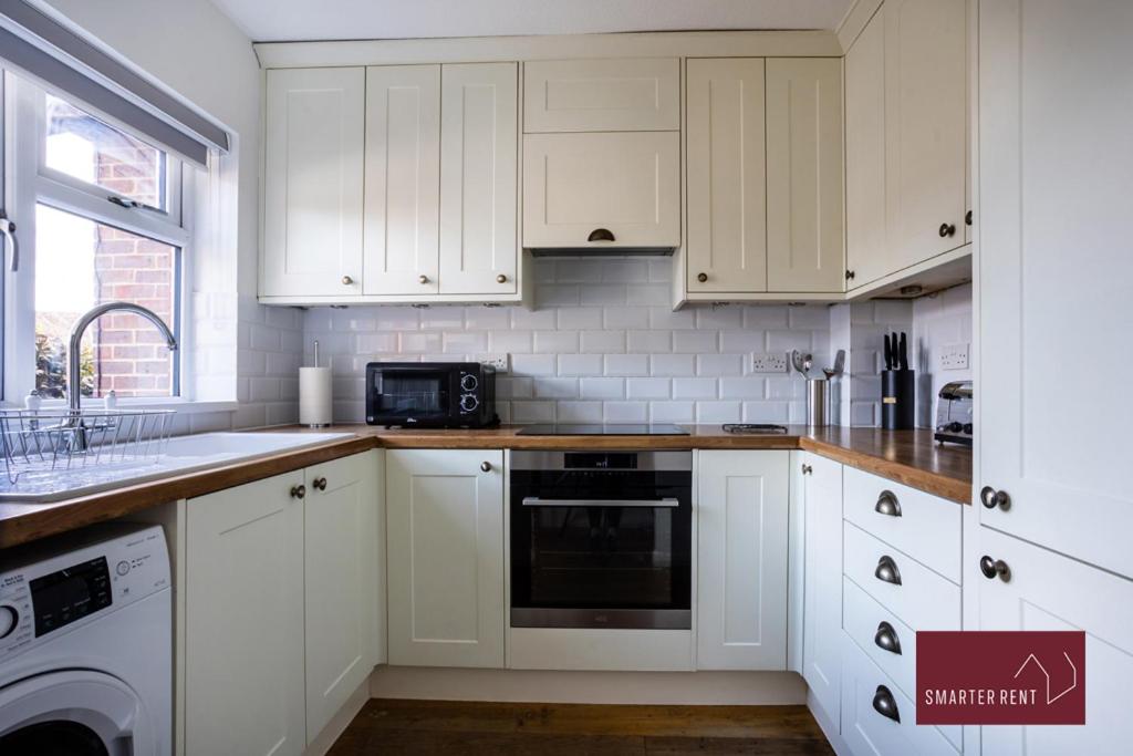 a white kitchen with white cabinets and a sink at Bracknell - 2 Bedroom Home With Parking & Garden in Easthampstead