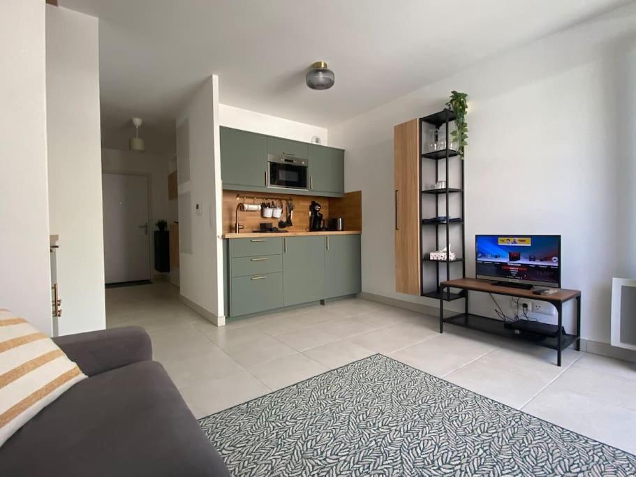 a living room with a couch and a kitchen with a tv at Studio des Pins neuf avec son garage fermé et son balcon in Villeneuve-lès-Maguelonne