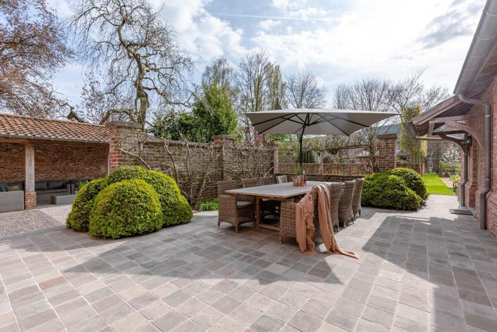 eine Terrasse mit einem Tisch und einem Sonnenschirm in der Unterkunft Huyze Termote - Top notch villa with wonderful garden in Wingene in Wingene
