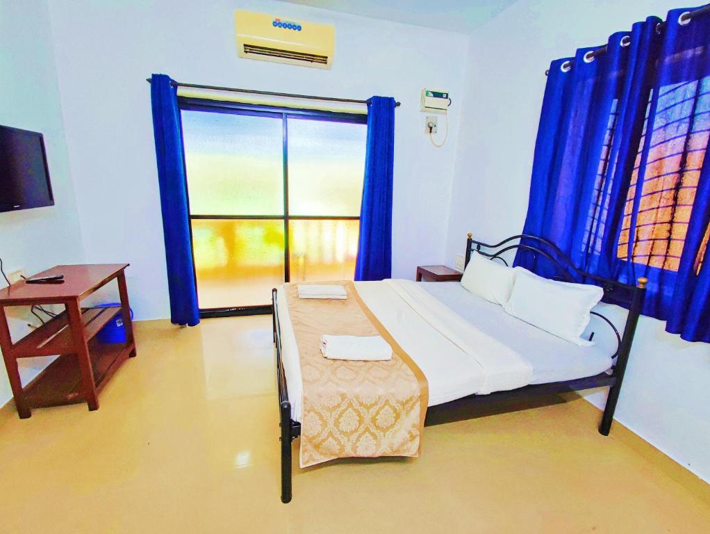 a bedroom with a bed and a window with blue curtains at Maria Comfort Stay in Calangute