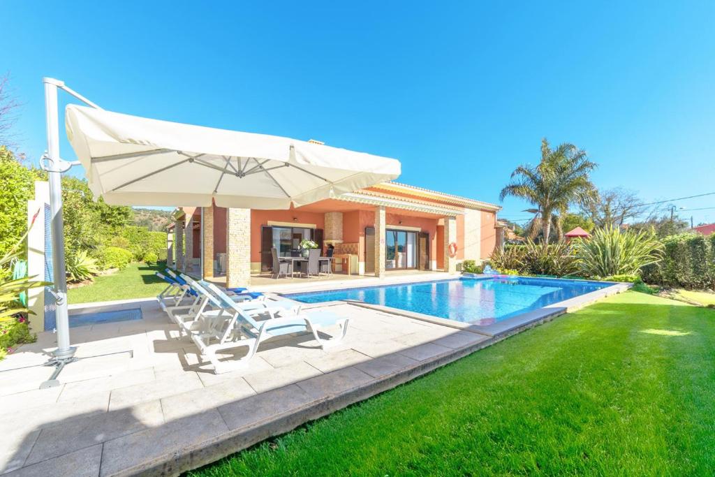 a house with a swimming pool and an umbrella at Villa Paraiso in São Bartolomeu de Messines