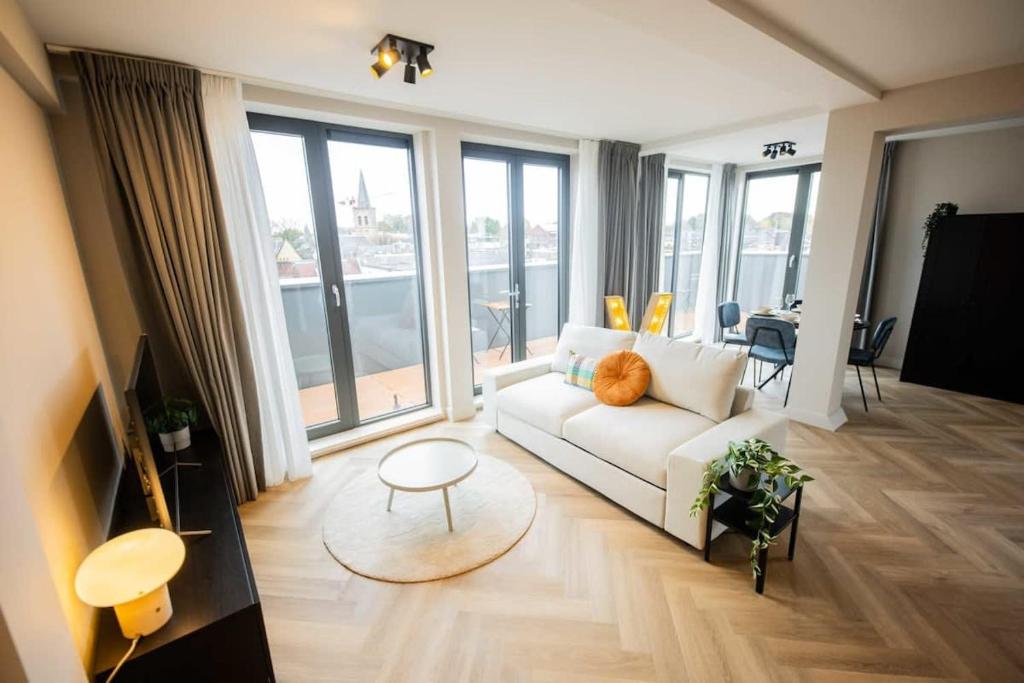 een woonkamer met een witte bank en grote ramen bij Alphabet Studio Apartments Penthouse KS71 in Hilversum