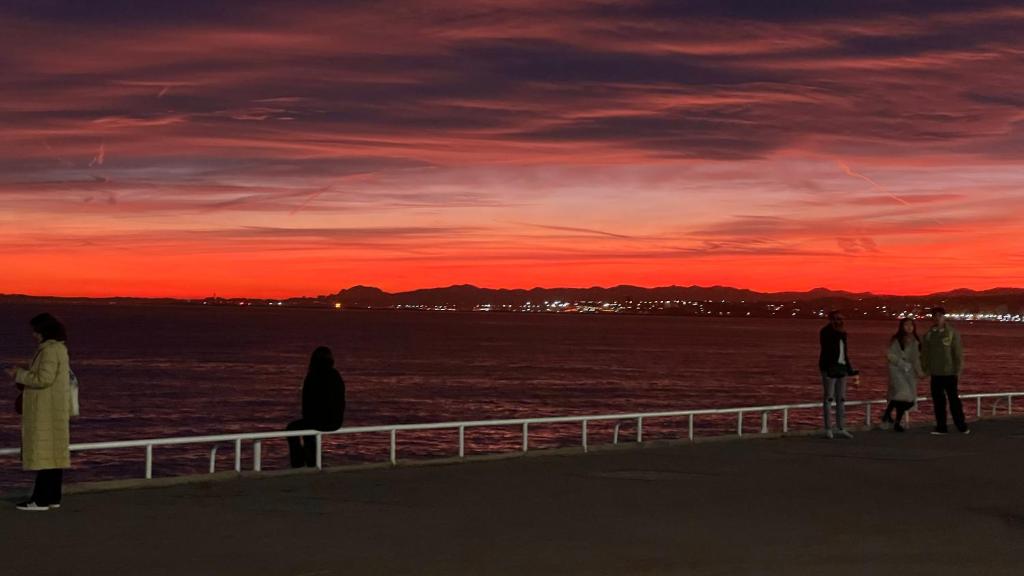 eine Gruppe von Menschen, die bei Sonnenuntergang auf einem Pier stehen in der Unterkunft Le Richemond - 50m de la MER in Nizza