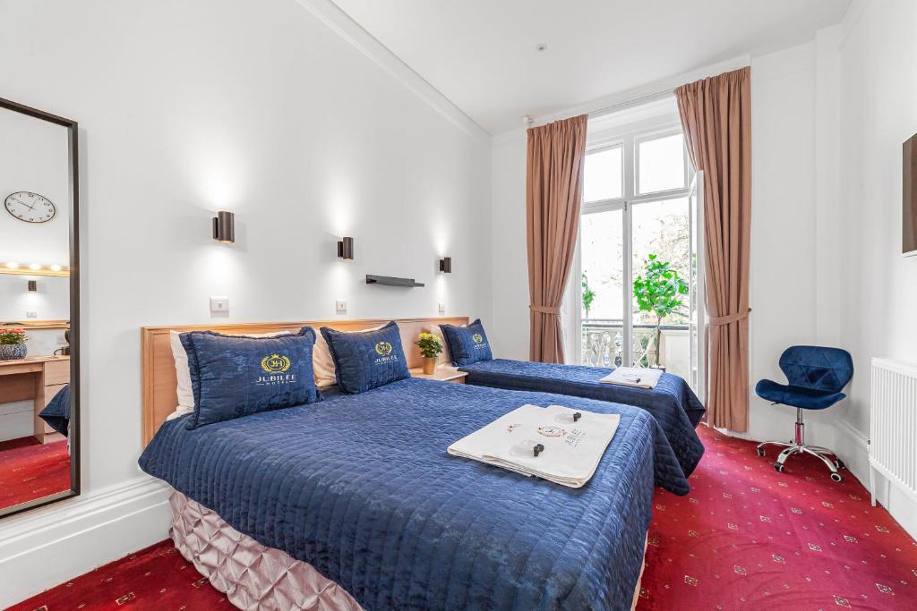 a bedroom with two beds with blue sheets and a window at Jubilee Hotel Victoria in London