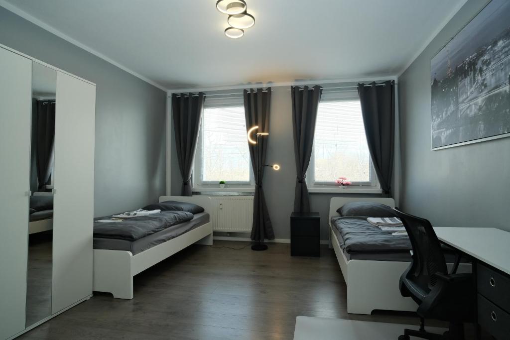 ライプツィヒにあるFit&Chill Apartment Sport, Entspannung & Netflixのベッド2台、デスク、窓2つが備わる客室です。