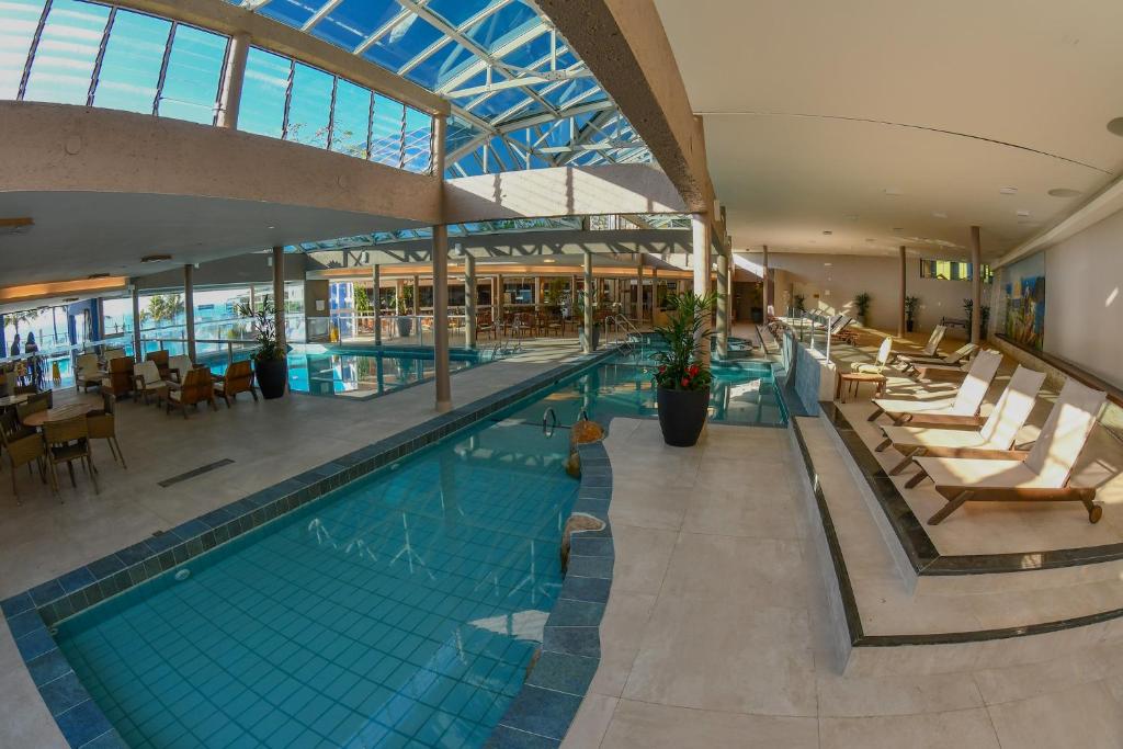 a large swimming pool in a building with chairs and tables at Costao do Santinho Resort All Inclusive in Florianópolis