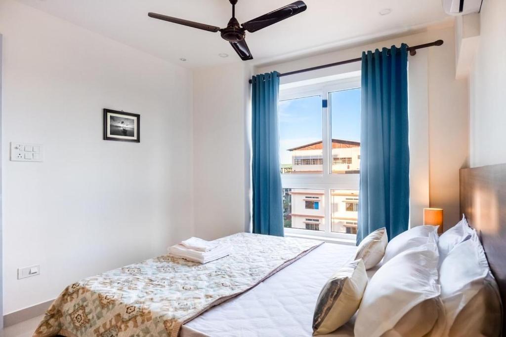 1 dormitorio con 1 cama con cortinas azules y ventana en Borail Homes, en Silchar