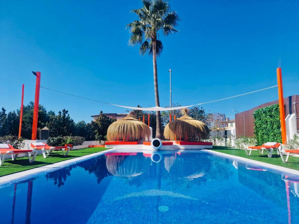 a swimming pool with straw umbrellas and a palm tree at Villa Dolce Vita in Marratxí 